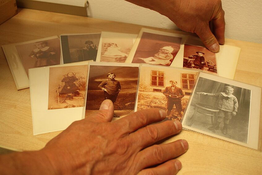 eine Hand breitet Fotos auf auf einem Tisch aus